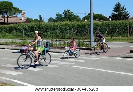 family with mom and two children cross the street in the crosswalk on bike