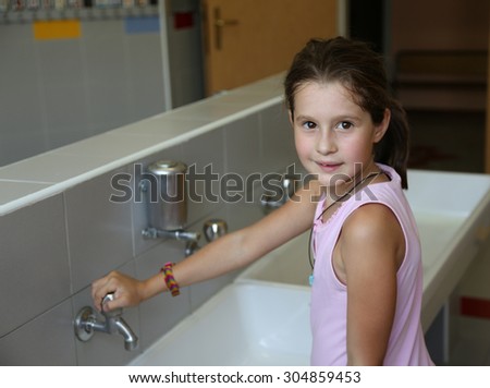 little girl washing hands in the ceramic sink in the bathroom  of school