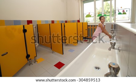 smiling girl washing her hands in the sink in the bathroom of the school