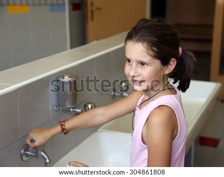 little girl is washing her hands in the sink in the bathroom of the school