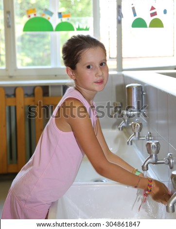 pretty little girl washing hands in the ceramic sink in the bathroom  of school