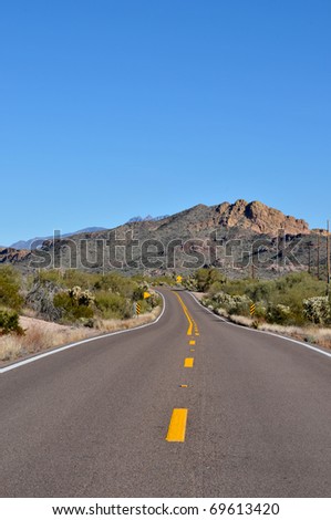 Rural highway through the Arizona desert with lots of cacti and mountains in the background