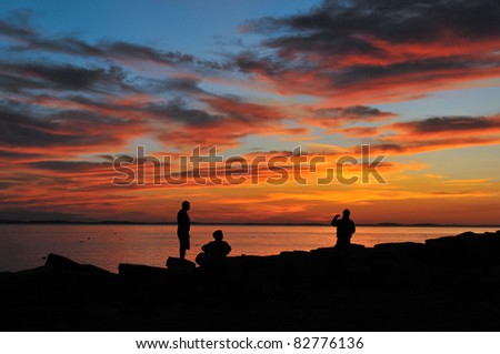 Friends silhouetted against a glorious orange sunset at Lane\'s Cove in Gloucester, MA