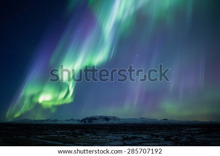 Strong bright purple green aurora noprthern lights over mountain lava plain, Thingvellir, Iceland