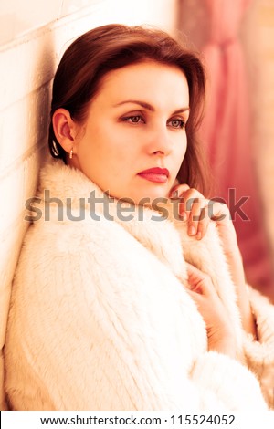 Beautiful woman in a fur jacket sits against the wall