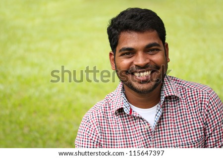 Closeup photo of attractive, handsome & smart south-asian/indian entrepreneur with smiling expression. The person is wearing a formal shirt & the picture is shot with beautiful lawn in the background