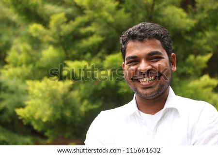 Close-up image of happy, excited & handsome asian/indian man with smile. The person is wearing a white shirt & the picture is shot in natural settings
