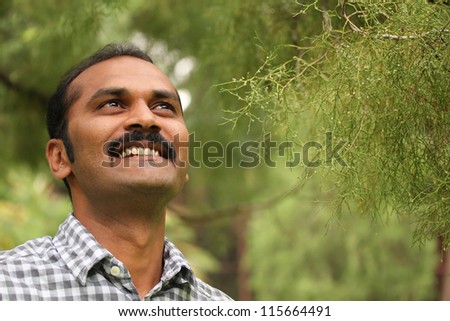 Close-up photo of hopeful, relaxed & happy asian/indian man looking confidently ahead. The executive is wearing a formal shirt & the picture is shot in natural settings
