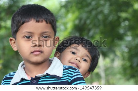 Indian boy & girl ( brother and sister ) playing & enjoying in a park. This summer time photo is of two beautiful kids sitting together in a garden which is seen in the background