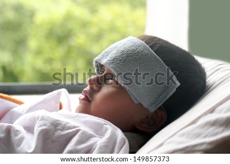Young indian boy ( child ) down with fever & illness in hospital. A wet cloth is kept on forehead to reduce the temperature
