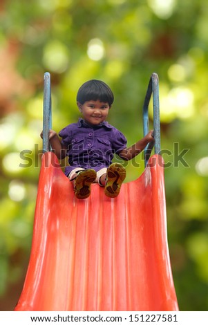 Beautiful & happy indian girl ( kid ) on park slider on a summer day. This girl\'s photo is on green background with clipping path showing summer time playground & a schoolgirl playing on a slider