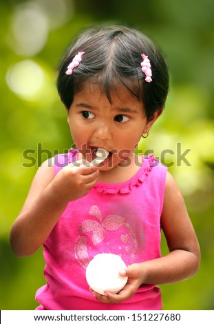 beautiful young indian girl child enjoying ice cream in a park. The photo shows female kid in pink dress smiling and relishing a scoop of ice cream