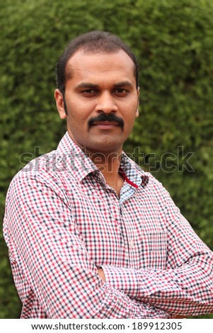 Portrait of handsome smiling indian executive or employee with bald head standing against green background. The photo is of a middle aged manager or team leader with arms crossed