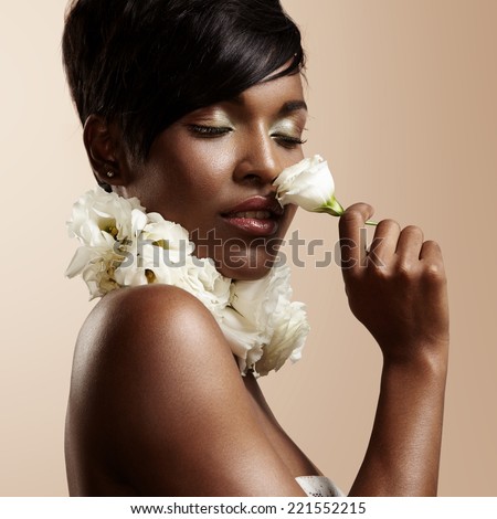 black woman with ideal skin and closed eyes sniffing a flower
