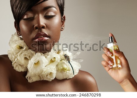 beauty black woman with flowers on her neck and a hand with a perfume bottle