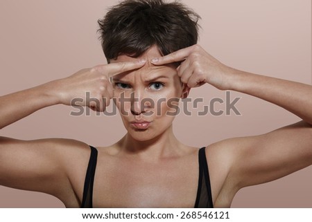 pretty girl with ideal skin squeezing pimple, beige back
