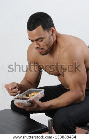 Male fitness Model eating healthy bodybuilding diet food out of tupperware and jug of water