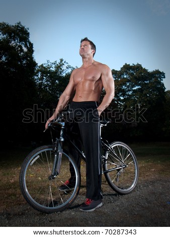Man with shirt off resting on mountain bike.  Thinking and resting. showing six pack abs