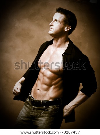Man in studio with shirt on but showing six pack abs.  Fitness model type physique.  Sepia toned.