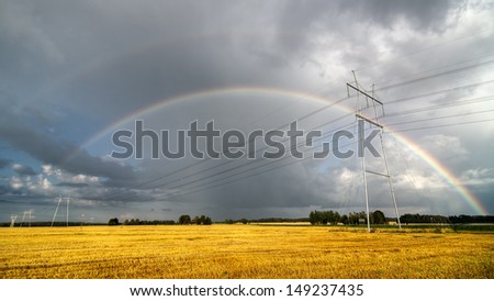 harvested crop field with power lines and rainbow