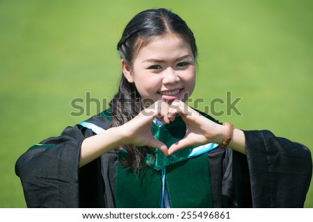 a pretty young female graduate happy and make the heart with two hands