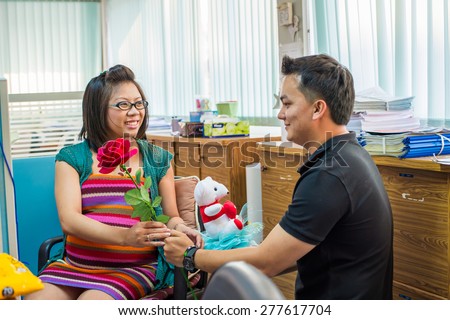 the nice husband gave the red flower to a pretty Asian pregnant and say he love her very much in the office