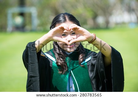 an Asian pretty young female graduate making heart with two hands in front of her face