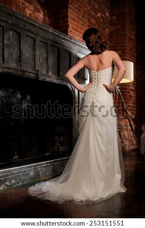 Bride in wedding dress in the studio next to the fireplace with his back