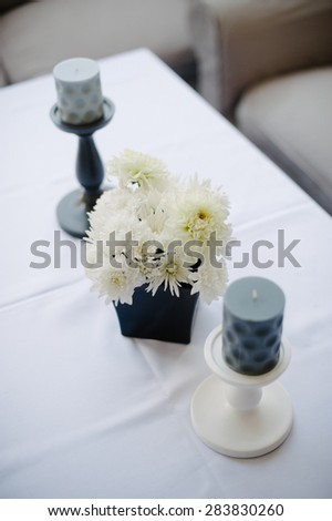 Flower vase in the shape of a cube and candlesticks standing next to the table ready to receive guests of the wedding ceremony.