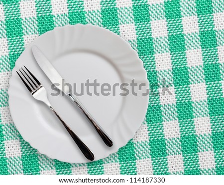 Plate with silverware on checkered green  background