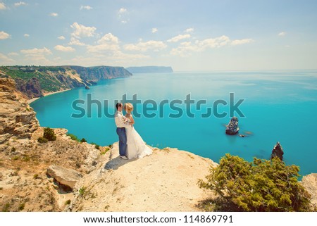 wedding theme: the bride and groom standing on a cliff near the azure waters. Groom in sunny summer day at the top of the bride hugging the mountains.