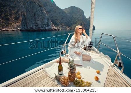 beautiful young girl eating and talking on a mobile phone on a boat sailing along the rocky shore of the sea