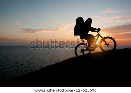 evening silhouette of a man climbing a mountain tourist on a bike