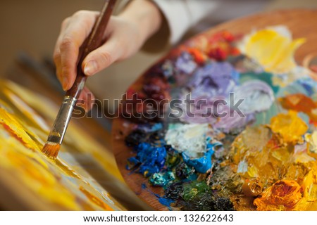 artist paints a picture of oil paint brush in hand with palette closeup
