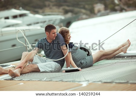 Young happy couple husband and pregnant wife sitting on a yacht at sea back to each other.