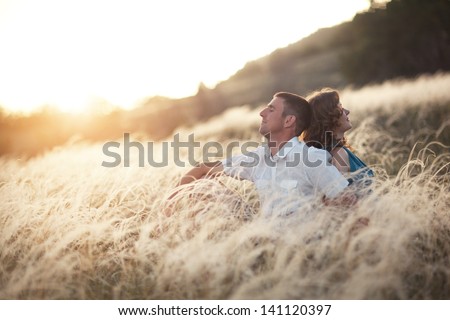 couple of lovers man and woman sitting back in a field at sunset