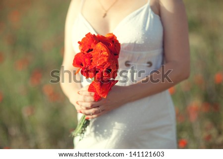 Bouquet of poppies in the hands of a woman in a white dress in a field
