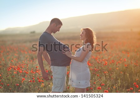 Funny happy pregnant couple walking a wild flower field outdoors.