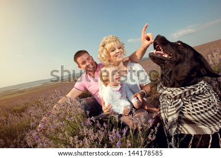 happy family mother father and daughter vacation in the field in the grass with a black labrador dog. family portrait