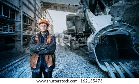 worker in a helmet stands near a big excavator crossed arms
