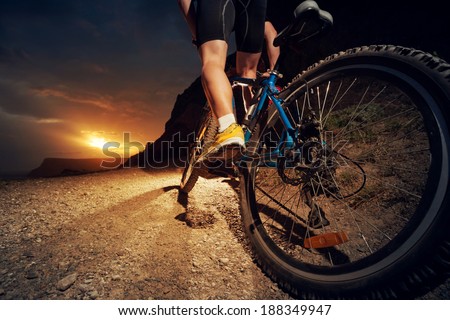 Man on mountain bike rides on the trail on a beautiful sunset. Bicycle wheel closeup.