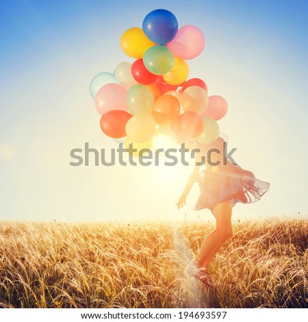 Girl with balloons running on the field to the sun at sunset.