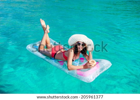 Woman relaxing on the swimming mattress in sunglasses and a hat and drinking coconut. Water activities.