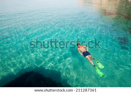 Young man snorkeling in clean water over coral reef. Top view of the swimmers with flippers, mask and snorkel.