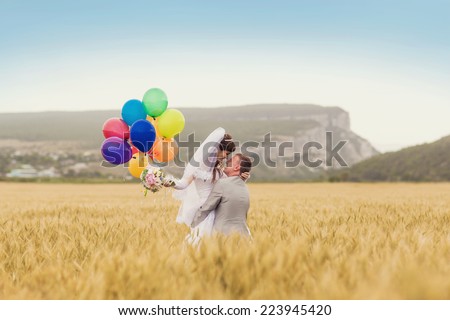 Wedding couple hugging and kissing outdoors in a field with balloons. Bride and groom standing in the grass of wheat.