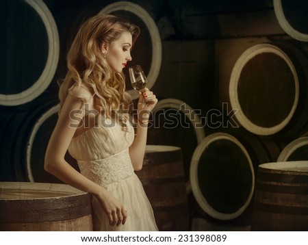 Beautiful woman with wine glass and bottle in the wine cellar on the background of the barrels. Degustation.