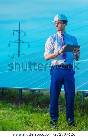 Solar power plant. Worker with the tablet stands in full length on a background of photovoltaic panels. Renewable energy sources.