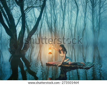 Woman with lantern floating on the lake in the misty forest in rustic dress. Beautiful fairy tale.