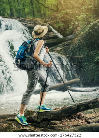 Hiker woman with backpack walking on a forest trail in the mountains on the background a waterfall. Hiking. Adventure in the forest.