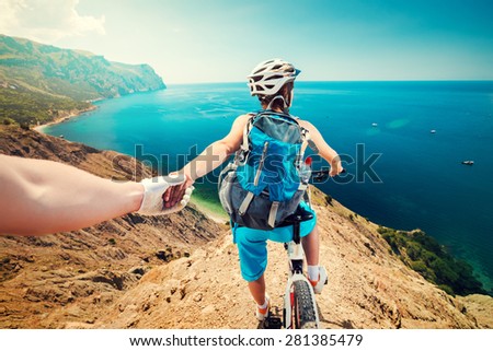 Woman on a bicycle holding his hand on the top of a mountain with beautiful scenery. Downhill bike.